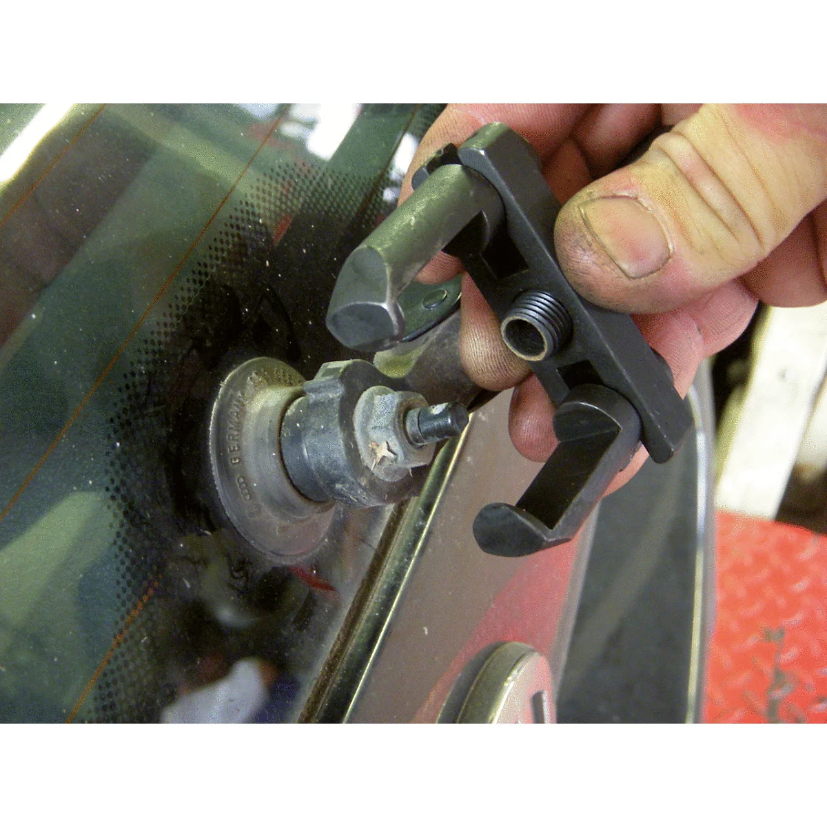 Eine Hand hält ein schwarzes Werkzeug, das an einem Metallstift an der Windschutzscheibe eines Fahrzeugs angebracht ist.